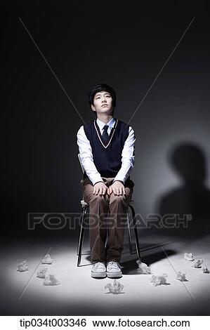 Stock Photograph - schoolboy sitting on the chair in a dark room. Fotosearch