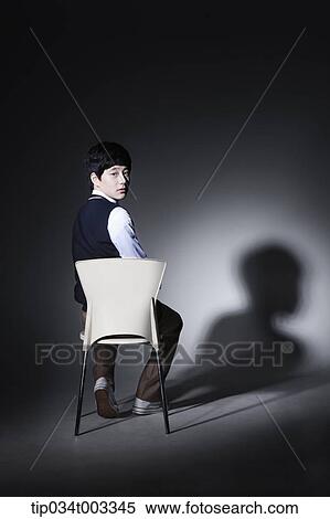 Stock Photography - schoolboy sitting on the chair in a dark room. Fotosearch