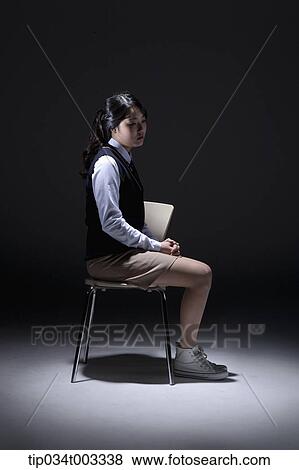 Stock Photo - schoolgirl sitting on the chair in a dark room. Fotosearch