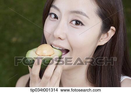 Picture - woman eating a half of avocado on her hands . Fotosearch