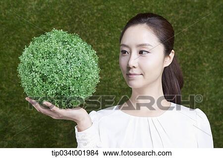 Picture - woman holding a sphere covered with grass. Fotosearch