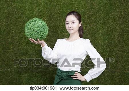 Stock Image - woman holding a sphere covered with grass. Fotosearch