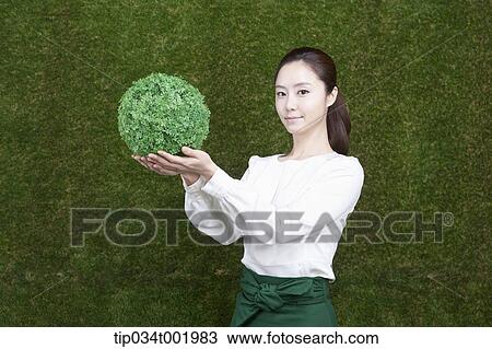 Stock Image - woman holding a sphere covered with grass. Fotosearch