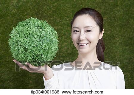 Stock Photograph - woman holding a sphere covered with grass. Fotosearch