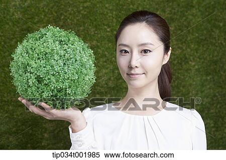 Stock Photography - woman holding a sphere covered with grass. Fotosearch