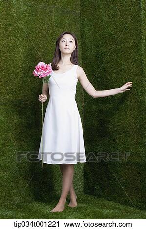 Stock Image - woman holding pink flower in her bare feet. Fotosearch