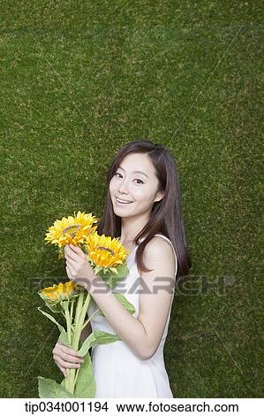 Picture - woman holding sunflower in her bare feet. Fotosearch