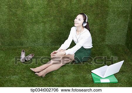 Stock Photograph - woman listening to music and reading a book in her bare feet. Fotosearch