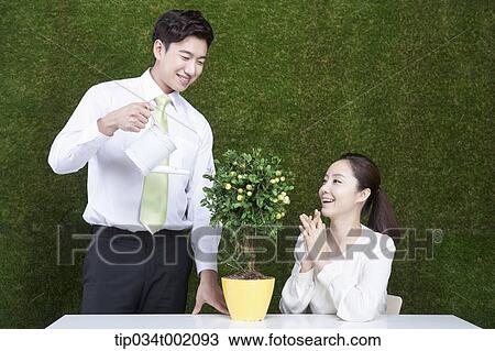 Stock Image - woman looking up the man watering the tree in the pot. Fotosearch