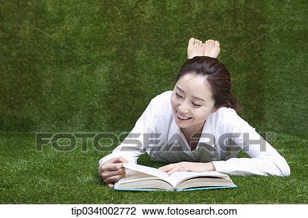 Stock Image - woman lying face and reading a book. Fotosearch