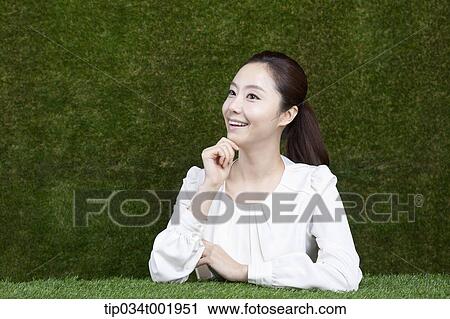 Stock Image - woman sitting and smiling with her chin propped on her hands. Fotosearch