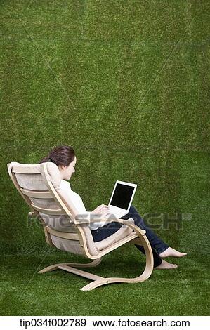Stock Photo - woman sitting on the armchair and using laptop. Fotosearch