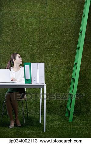 Stock Image - woman sitting on the desk and looking at the ladder . Fotosearch