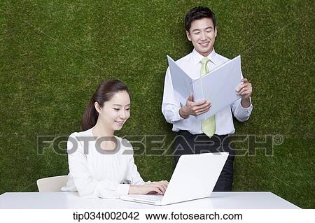 Stock Image - woman using computer and man holding a folder. Fotosearch
