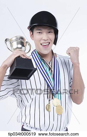 Stock Photo - A baseball player with gold medals and trophy. Fotosearch