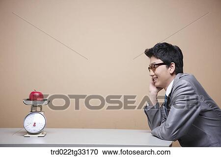 A businessman looking at an apple on the scale View Large Photo Image Stock Image - A businessman looking at an apple on the scale. Fotosearch