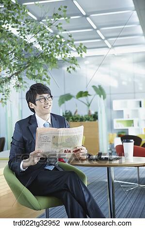 Stock Image - A businessman reading a newspaper in the lounge. Fotosearch