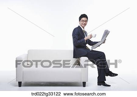 Stock Image - A businessman reading a newspaper on the couch. Fotosearch