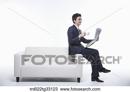 Stock Image - A businessman reading a newspaper on the couch. Fotosearch