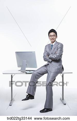 Picture - A businessman sitting on the desk with his arms folded. Fotosearch