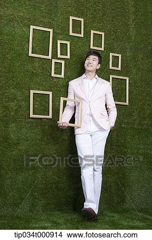 Picture - A man holding a frame from the green wall. Fotosearch