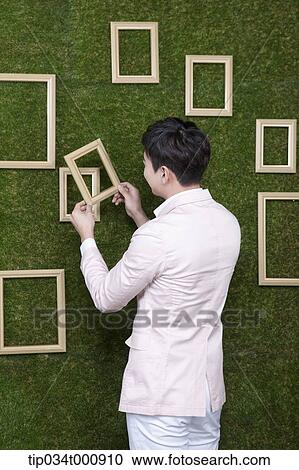 Stock Image - A man holding a frame from the green wall. Fotosearch