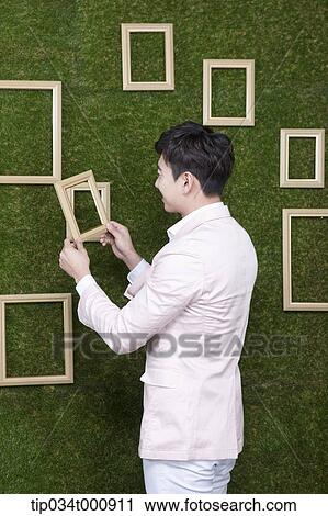 Stock Image - A man holding a frame from the green wall. Fotosearch