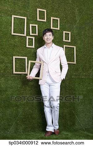 Stock Image - A man holding a frame from the green wall. Fotosearch
