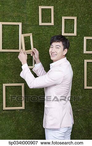 Stock Photo - A man holding a frame from the green wall. Fotosearch