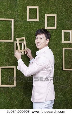 Stock Photo - A man holding a frame from the green wall. Fotosearch