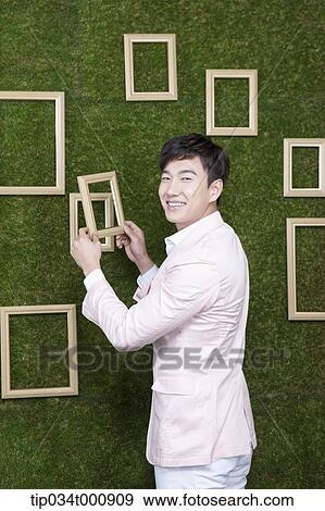 Stock Photo - A man holding a frame from the green wall. Fotosearch