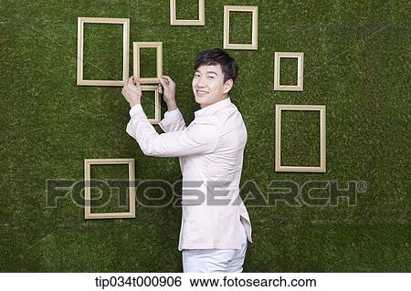 Stock Photograph - A man holding a frame from the green wall. Fotosearch