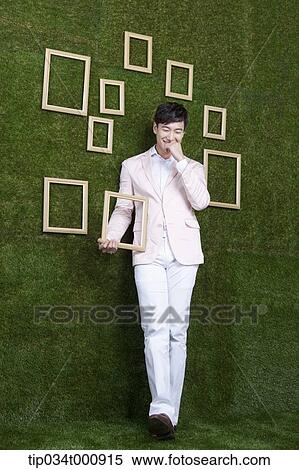 Stock Photography - A man holding a frame from the green wall. Fotosearch