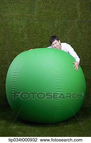 Stock Image - A man hugging a green ball. Fotosearch