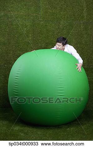 Stock Image - A man hugging a green ball. Fotosearch