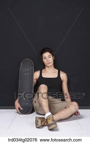 Stock Photograph - A man sitting with a skateboard. Fotosearch