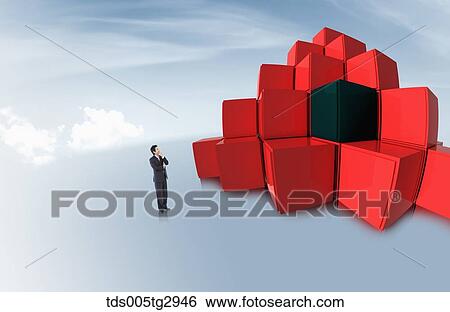 Stock Photograph - A man standing at piled red and black boxes . Fotosearch