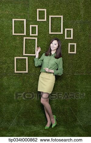 Stock Image - A woman and wooden frames on the green wall. Fotosearch