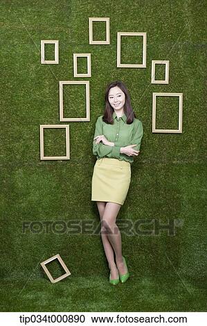 Stock Image - A woman and wooden frames on the green wall. Fotosearch