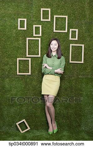 Stock Image - A woman and wooden frames on the green wall. Fotosearch