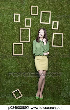 Stock Image - A woman and wooden frames on the green wall. Fotosearch