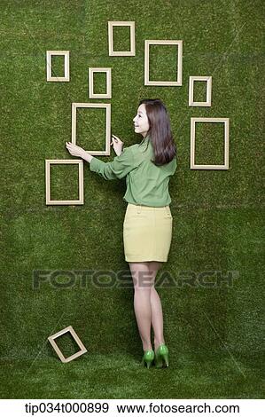 Stock Photo - A woman arranging the frame on the green wall. Fotosearch