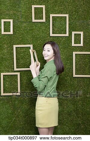Stock Photo - A woman holding a frame from the green wall. Fotosearch