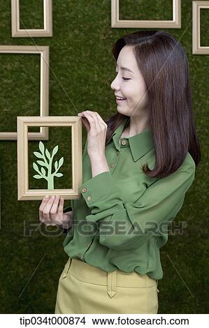 Picture - A woman holding a frame of green tree. Fotosearch