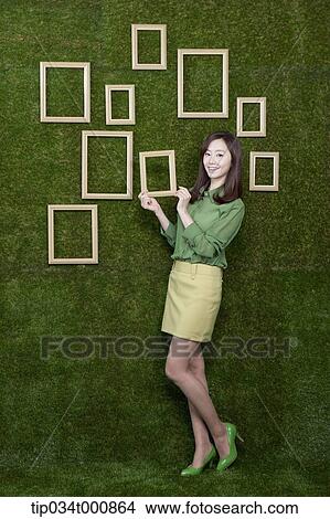 A woman holding a wooden frame from the green wall View Large Photo Image Picture - A woman holding a wooden frame from the green wall. Fotosearch