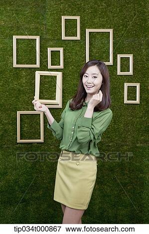 Stock Photo - A woman holding a wooden frame from the green wall. Fotosearch