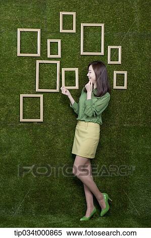 Stock Photography - A woman holding a wooden frame from the green wall. Fotosearch