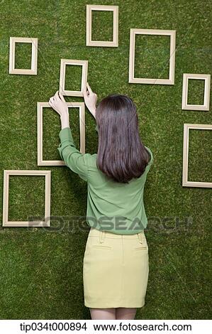 Picture - A woman putting the frame on the green wall. Fotosearch