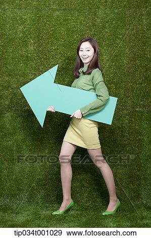 Stock Photo - A woman standing with a green arrow. Fotosearch