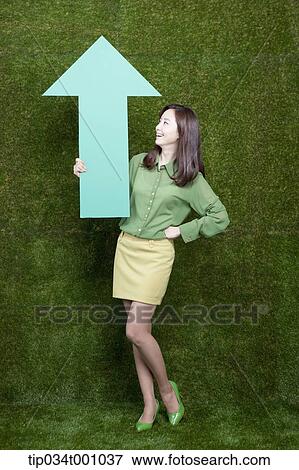 Stock Photo - A woman standing with a green arrow. Fotosearch
